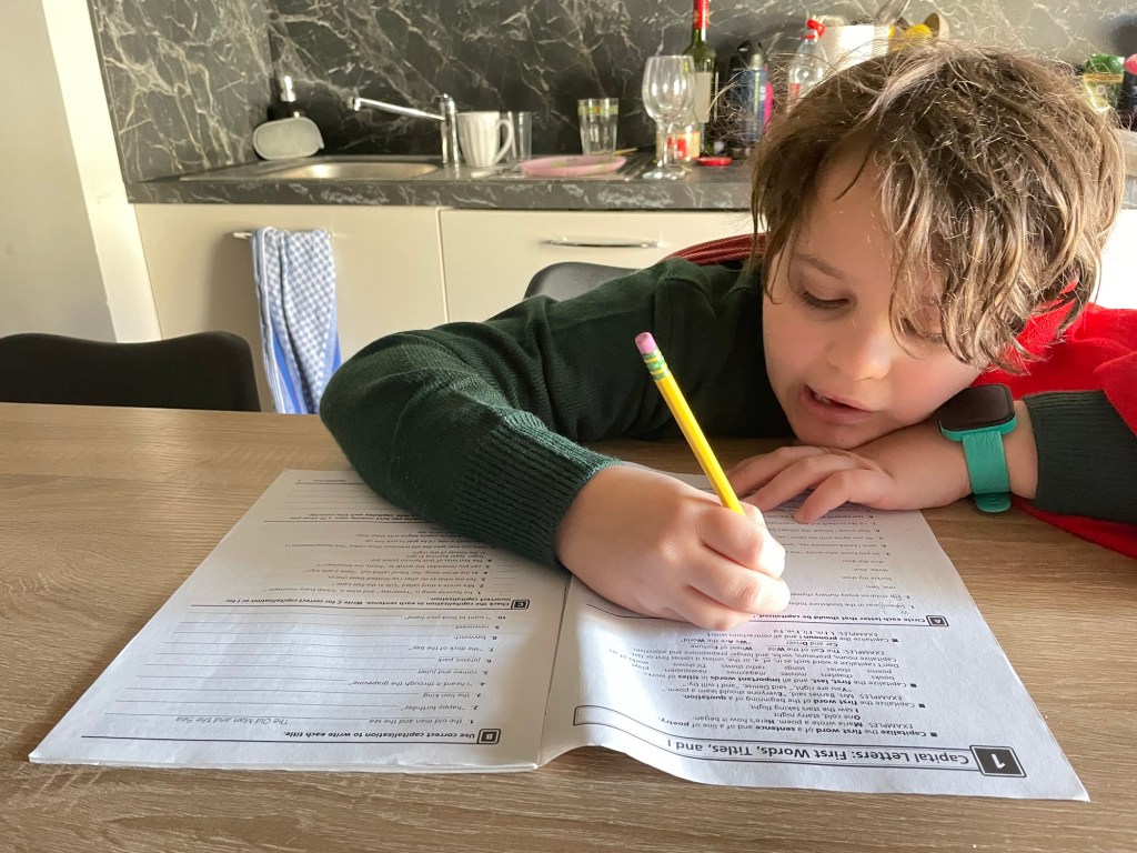A boy writes in a workbook with a pencil