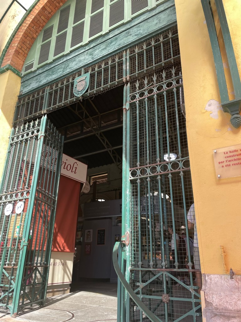 Big metal gates in a sunny wall lead to a dark cool interior with a hint of activity inside